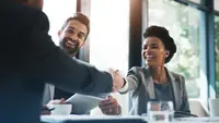 Happy couple at a table completing paperwork. Woman is shaking hands with the bank representative.