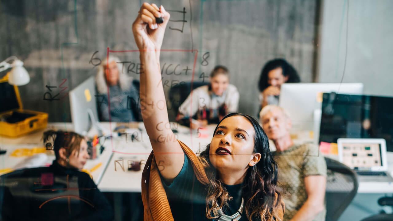 Businesswoman explaining strategy to colleagues while writing on glass at IT company
