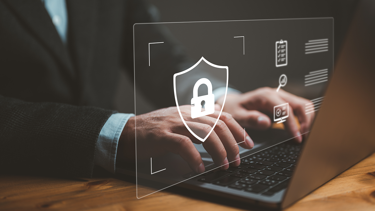 Closeup of hands typing on a computer with a security badge image layered on top